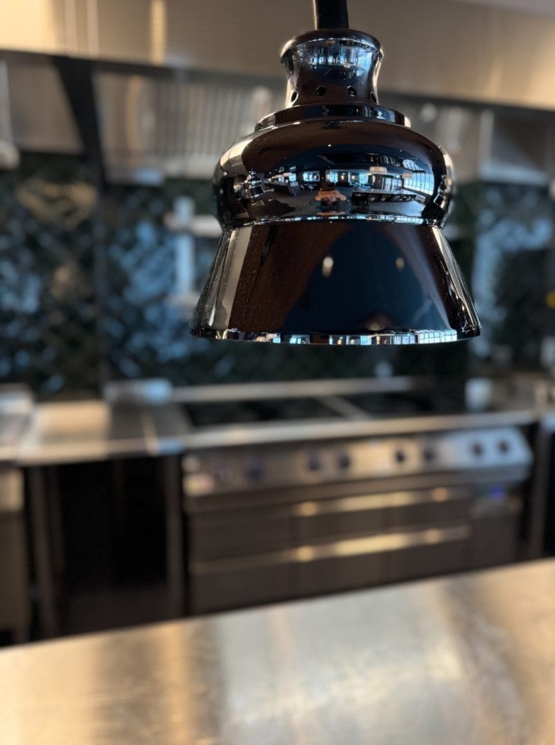 Varmelampe stayhot hengende over rustfri disk med koketopp og kjølebenk i bakgrunnen