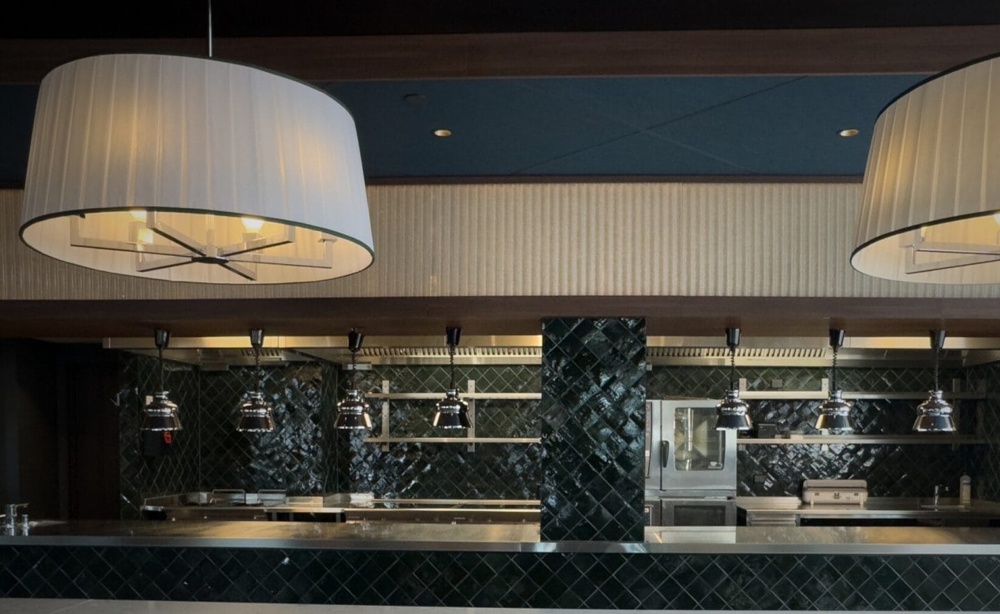 bredt storkjøkken med belysning og grønne fliser og storkjøkkenutstyr i bakgrunnen