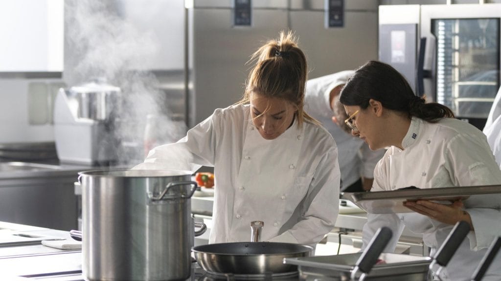 kokker ved storkjøkken som lager mat med kombidamper i bakgrunnen