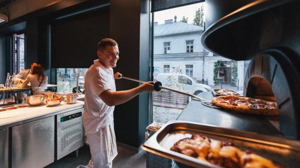 kokk på pizzeria som fører inn pizza i napolitansk pizzaovn